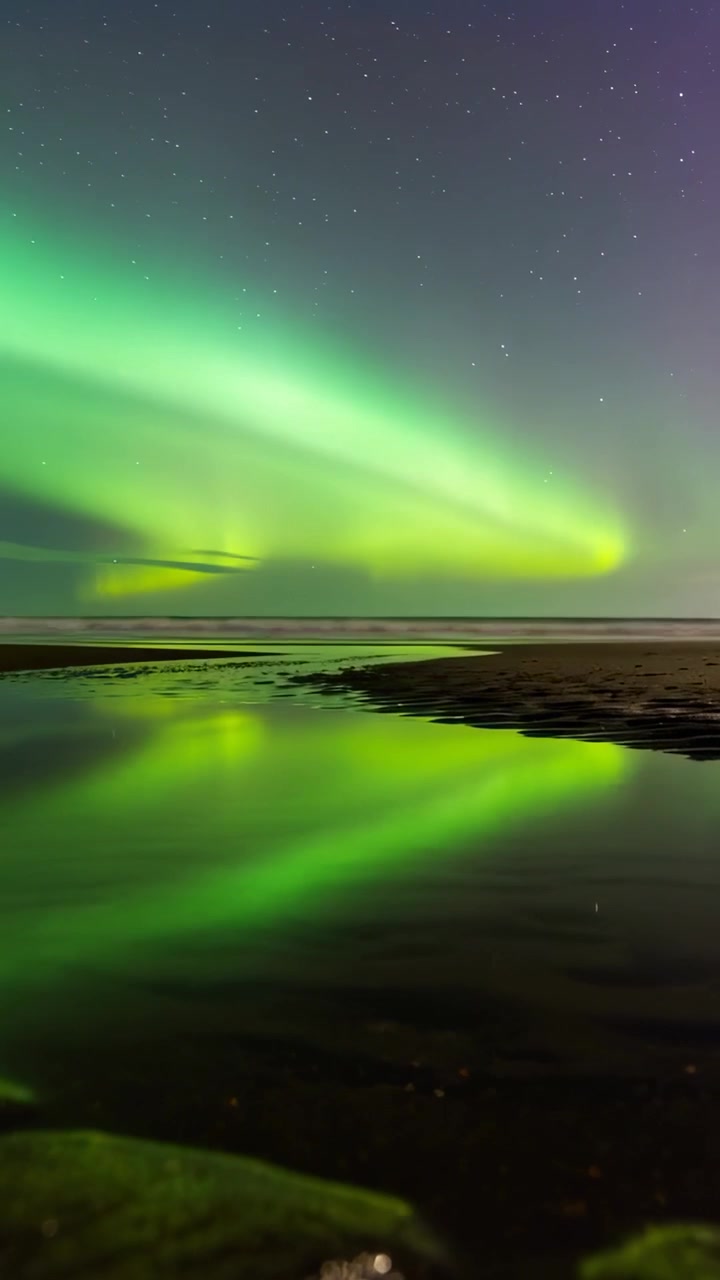 Video verticale: Aurora cangiante che si estende su una piana di marea di notte, spinta dal vento solare, con pozze riflettenti.