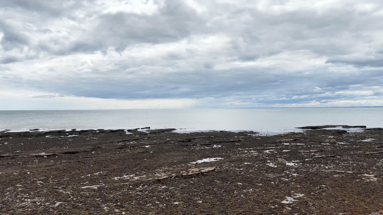 Wide-angle pan reveals rocky shore, tidal pools, and cloudy sky under soft natural lighting