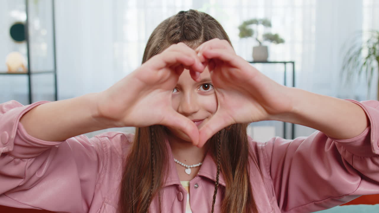 Niña romántica haciendo un símbolo de amor y mostrando un corazón a la cámara: solidaridad, gratitud, donación.
