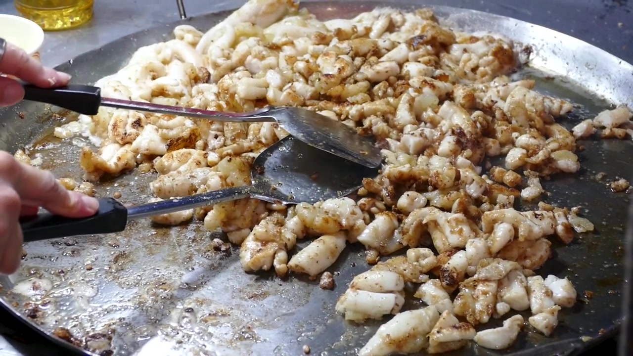 Venditore asiatico che cucina uova di calamaro fritte in una bancarella di street food