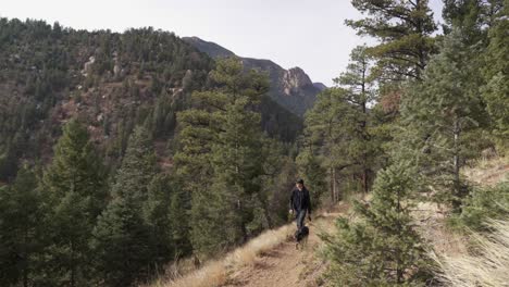 caucasian hiking man walks dog along mountain forest trail in colorado