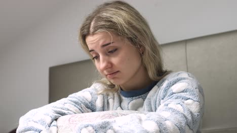 young woman feeling sad while sitting on bed