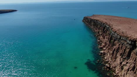 Aerial-view-moving-forward-tilting-up-shot,-Scenic-view-of-Isla-Espiritu-Santo-in-Baja-Sur,-Mexico,-emerald-green-sea,-sunlight-reflecting-on-the-sea-in-the-background