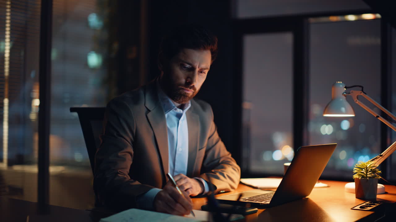 Serious businessman browsing computer writing notes at cozy dark flat closeup