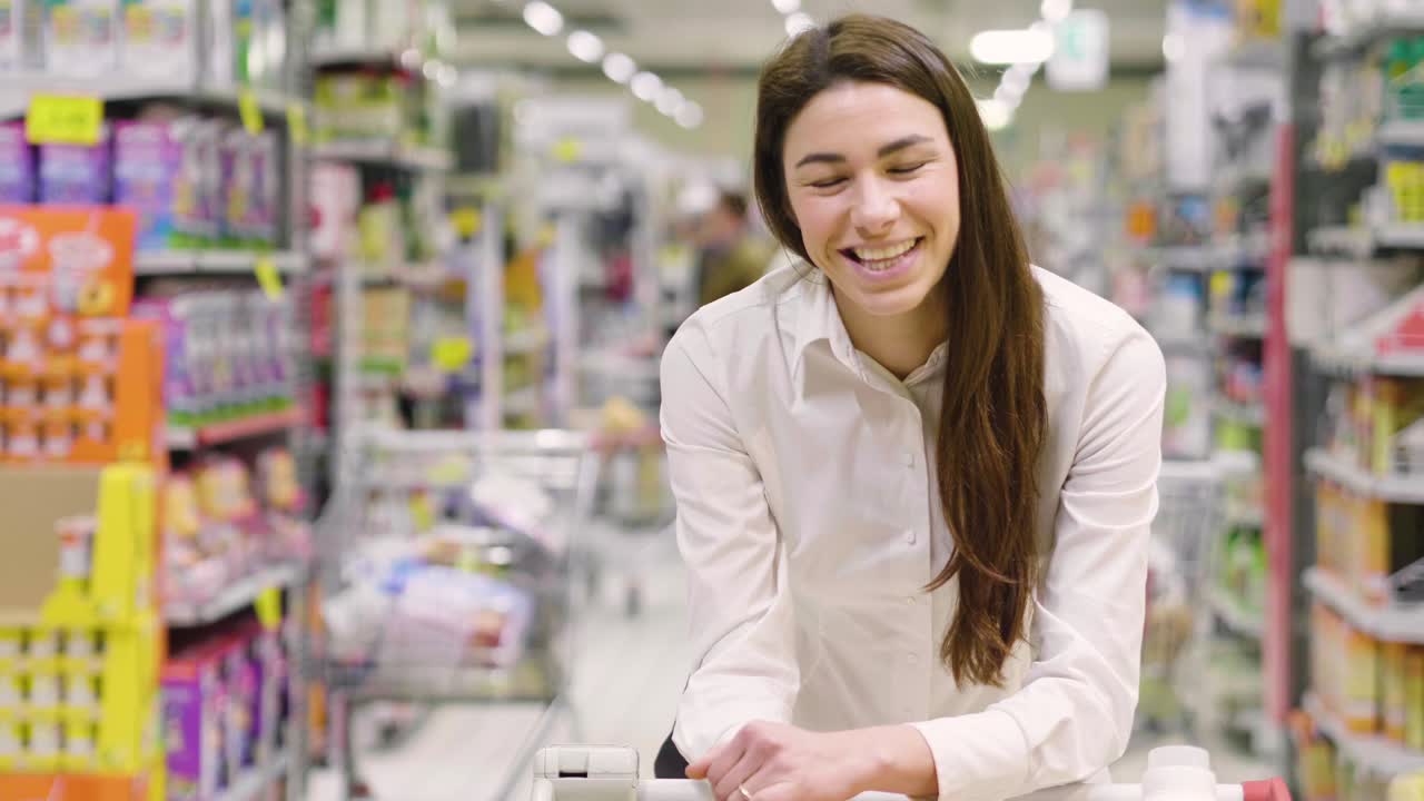 Una bella donna fa la spesa per la casa e compra prodotti alimentari, per la pulizia della casa e per la cura del corpo in un supermercato.