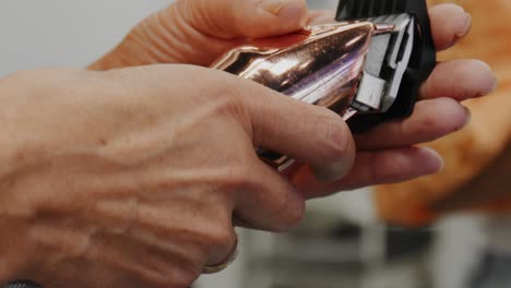 a female hair stylist is holding clippers and a guard for the clippers, then puts the clipper guard onto the rose gold clippers