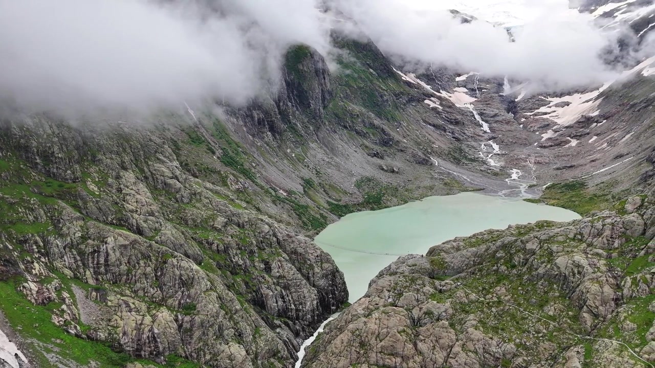Veduta aerea del ponte Trift, del suo lago e delle montagne nebbiose circostanti (Triftbrücke Triftgletscher), Berna, Svizzera