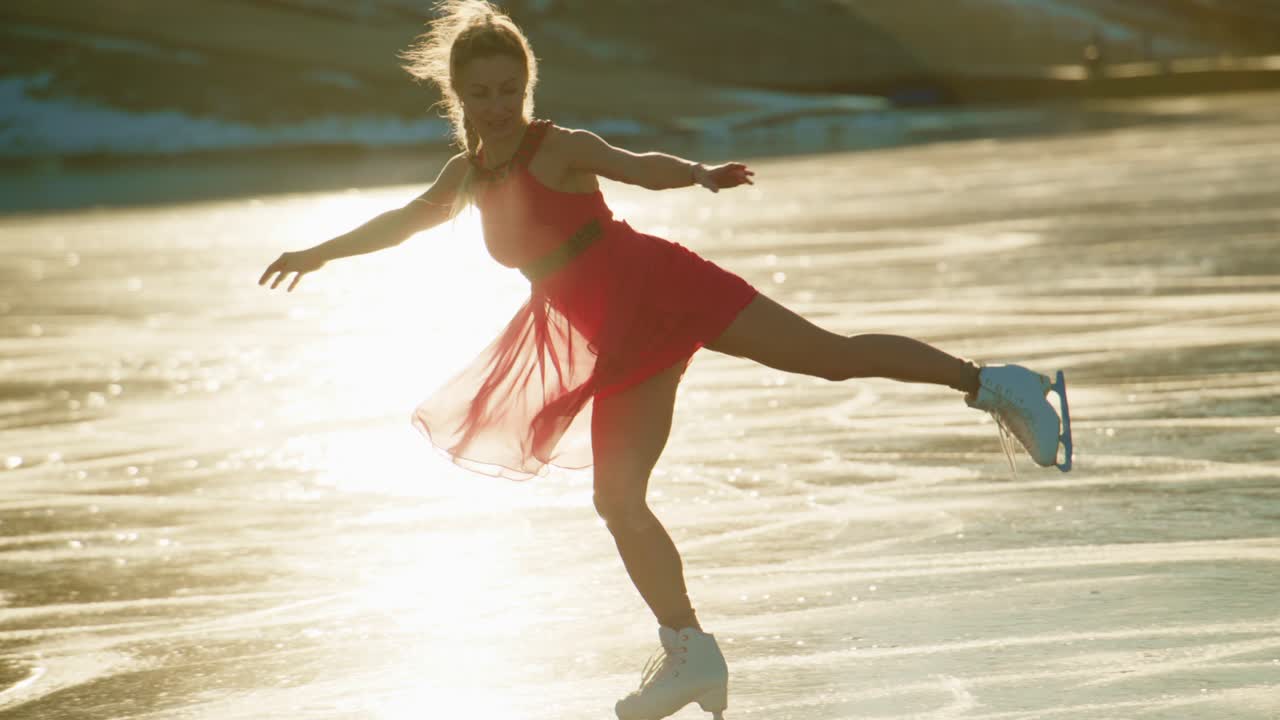 Anmutige Eiskunstläuferin im roten Kleid, die flinke Bewegungen auf einem atemberaubenden Wintersee mit glitzernder Eisfläche ausführt, brillant eingefangen in zwei Frames einer wunderschönen Videosequenz