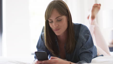 middle-aged caucasian woman lies comfortably at home, browsing her smartphone