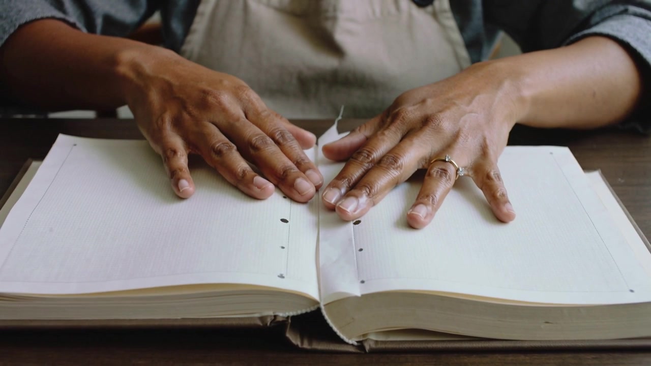 Pressant les mains sur une bande, lissant la couture du dos sur une table pour aplatir les pages, en tablier.