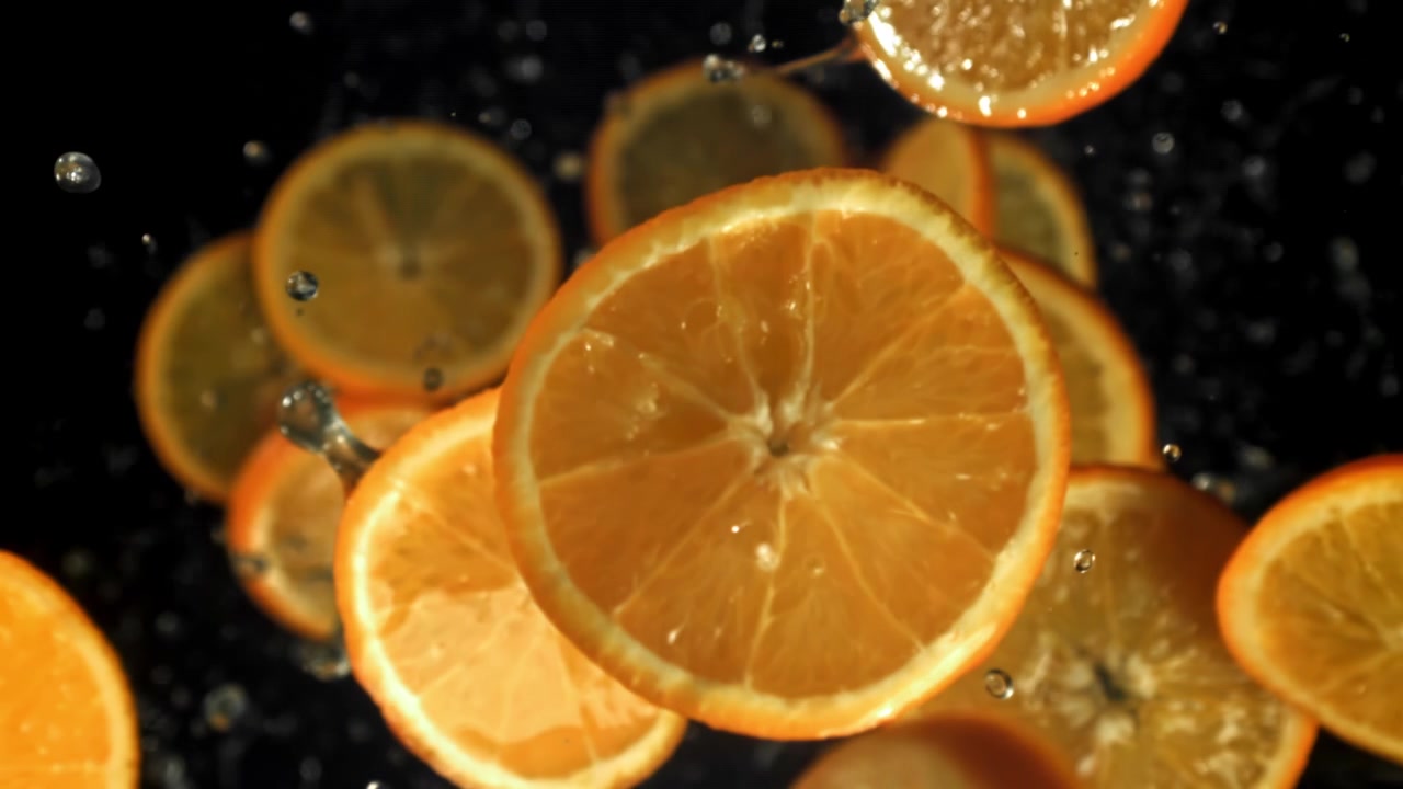 Frische Orangenscheiben fallen in Zeitlupe mit Wassertropfen