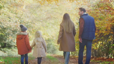 Rear-View-Of-Family-With-Parents-And-Children-Holding-Hands-Walking-On-Path-In-Autumn-Countryside