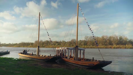 small wooden boats sit empty in the shade at side of idyllic riverbank