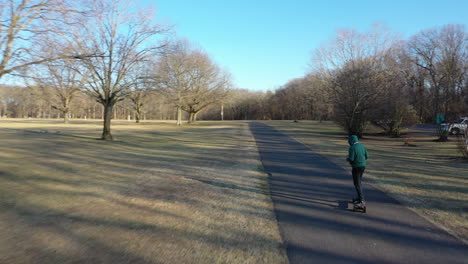 An-aerial-tracking-of-a-man-on-an-electric-skateboard-in-an-empty-park-on-a-sunny-day