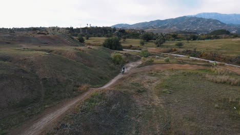 Aerial-static-shot-of-a-dry-and-dusty-motocross-track-in-Malaga-in-Spain-with-hills,-trees-and-mountains-in-the-background-while-a-motocross-rider-performs-a-dangerous-stunt