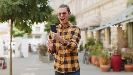 Happy-man-using-mobile-smartphone-on-city-street-celebrating-win-good-email-message-news-victory