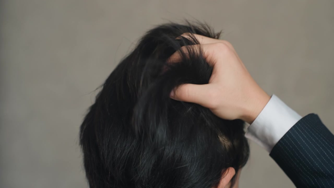 Pria merapikan rambut dengan jari, manset jas terlihat, close-up dari belakang kepala menunjukkan rambut hitam berkilau, kegugupan halus sebelum rapat saat eksekutif bersiap untuk presentasi, cahaya studio lembut dan netral
