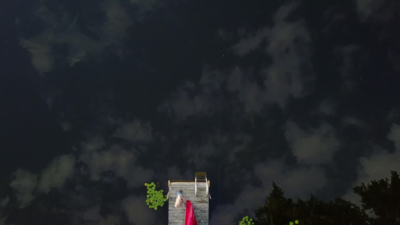 UHD Top down view of a man reeling in a fishing line and casting it from the dock in cottage country Ontario, Canada