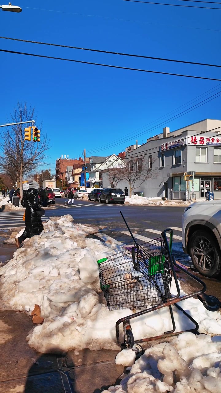 New York, USA, 25. joulukuuta 2025: Kaatunut ostoskärry lumessa Brooklynin risteyksessä. Metallikärry makaa sohjoisen lumivallin vieressä, pysäköityjä autoja, liikennevaloja