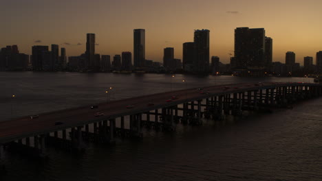 miami bridge with downtown miami in the background and cars going by at sunset, aerial shot