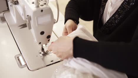 High-angle-view-of-female-hands-with-colored-manicure-in-process-of-creating-wedding-white-dress.-Clothes-designer-working-with