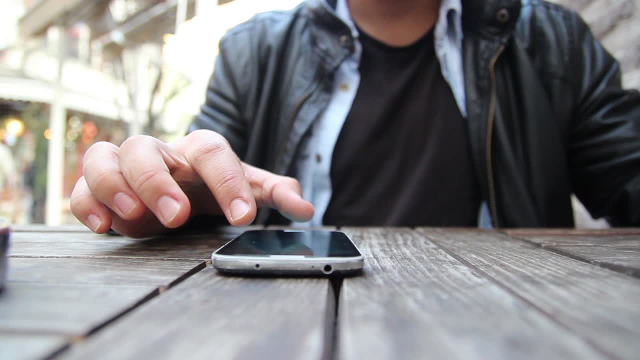 카페에서 스마트폰을 사용하는 젊은 남자가 손을  ⁇ 고 있습니다.