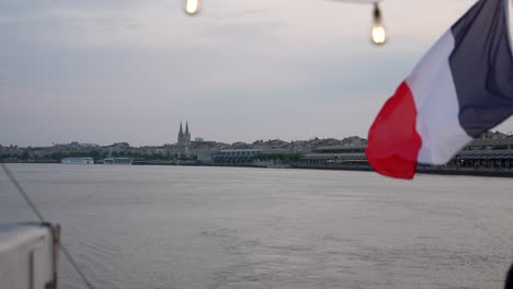 french flag waving on the back of a barge boat on the garonne river in bordeaux france at dusk, wide shot