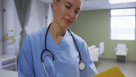 Caucasian-female-doctor-holding-medical-documentation,-smiling-to-camera-in-hospital-room