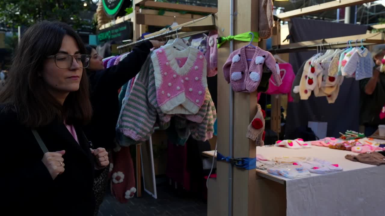 Woman Browsing Handmade Knitted Baby Cardigans at a Market Stall