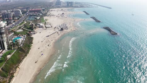 Largas-Olas-Del-Mar-Mediterráneo-Ruedan-Tranquilamente-Sobre-Las-Extensas-Playas-Mientras-Muchas-Personas-Disfrutan-De-La-Bonita-Playa-De-Verano-De-Nuevo-Detrás-De-Los-Rompeolas-En-Herzeliya-Israel