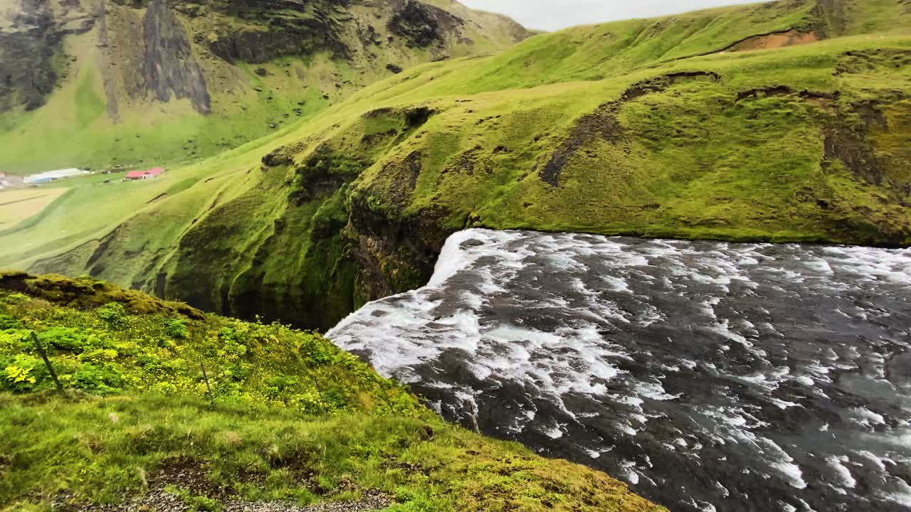 lentamente hacia la cascada de skogafoss que fluye por encima del borde del acantilado islandés desde el río skoga