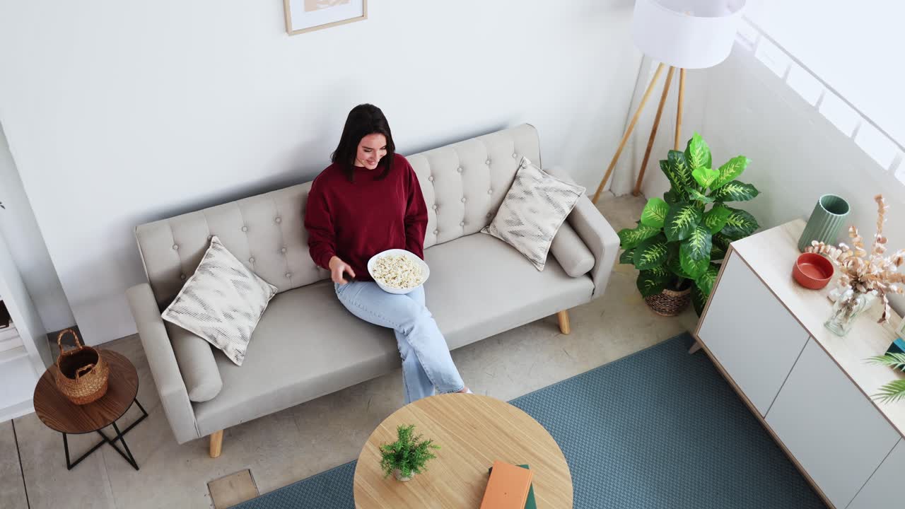 Ung kvinde slapper af på sofaen med popcorn og fjernbetjening
