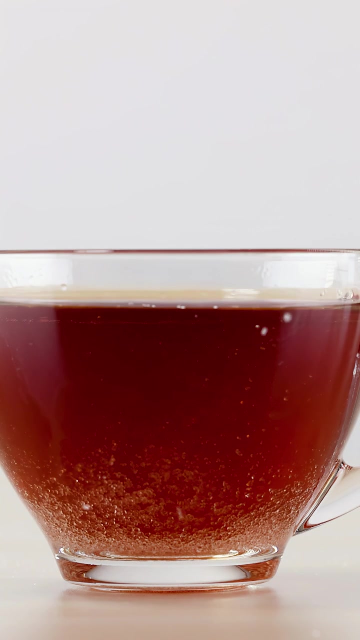 Primo piano di cristalli di zucchero che affondano e si dissolvono nel tè nero caldo in una tazza di vetro