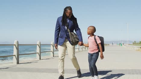 Video-of-happy-african-american-father-and-son-walking-and-talking-by-sea