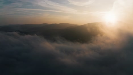 sunset fly above clouds in the morning lights with hills and fog and beautiful panoramic aerial view with a drone