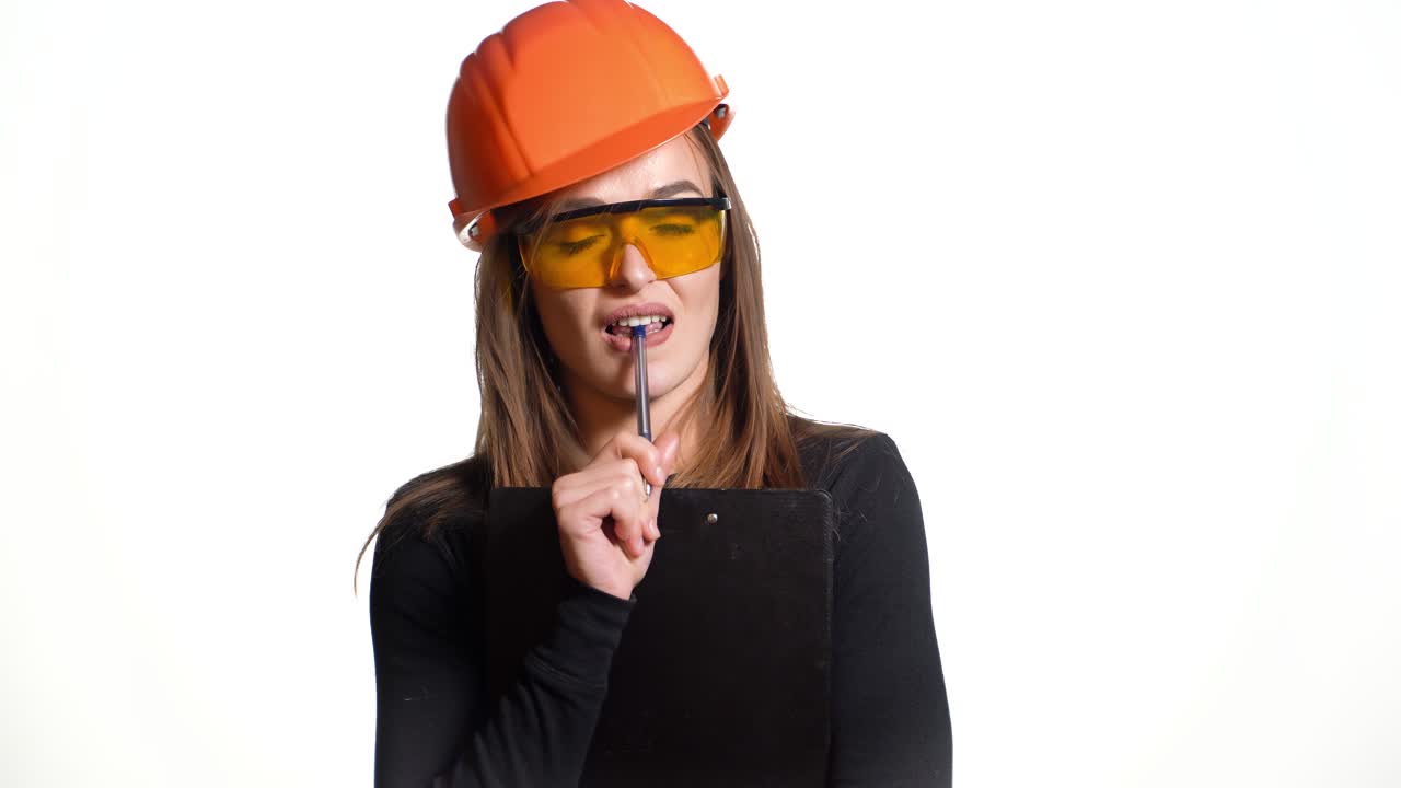Young woman construction worker in hard hat on a white background. Attractive woman builder with notepad in hand makes the decision