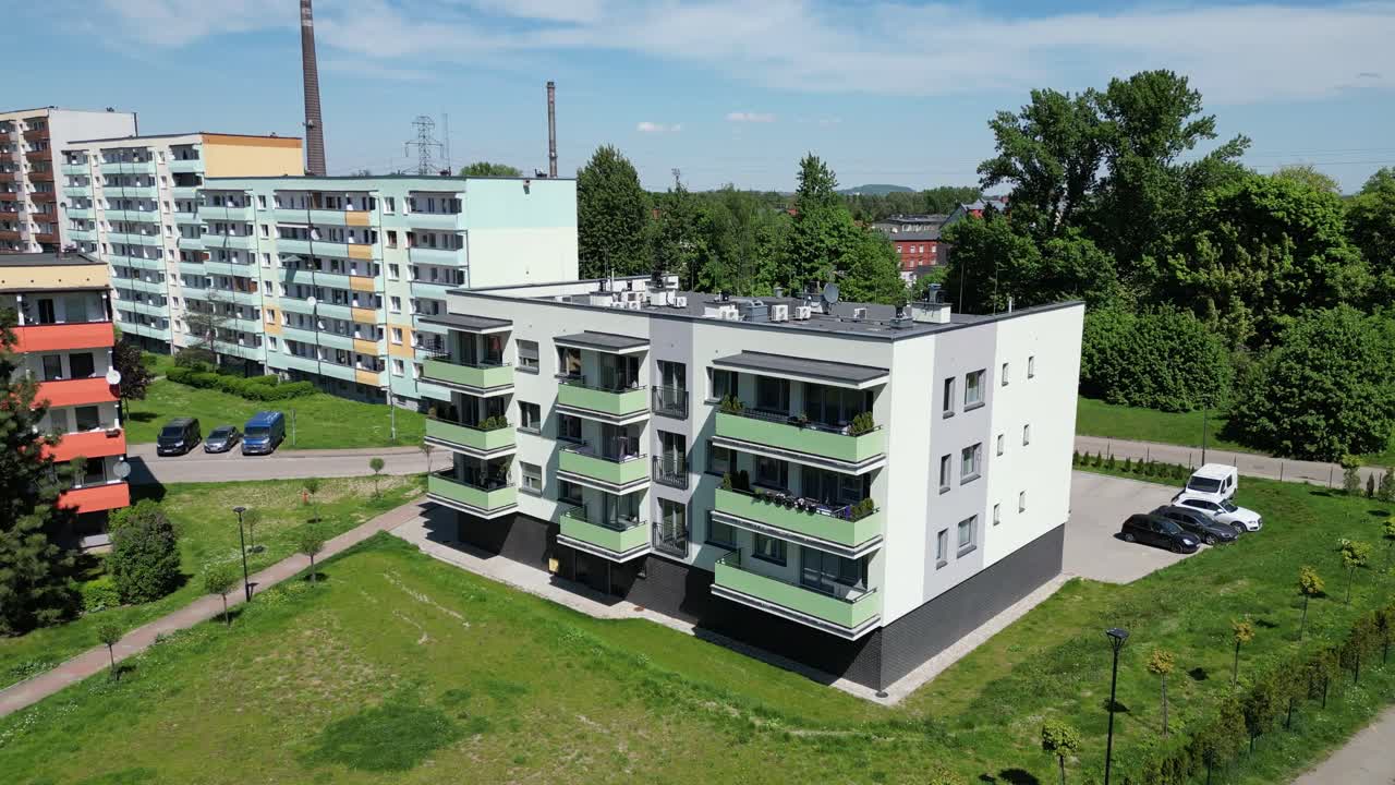 Zona residenziale con condomini durante una bella giornata estiva, circondata da una vegetazione rigogliosa, erba e alberi sotto un cielo blu