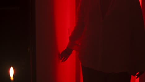 slow motion cinematic shot of a person in a white blouse stroking a wall with the hand, walks forward in an environment with red lighting and burning candles