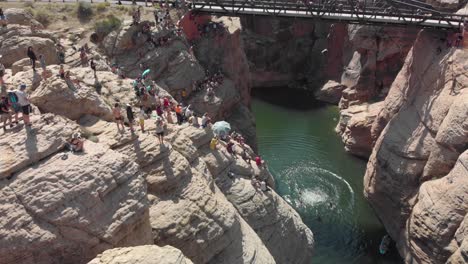crowd watches competing man jump into canyon creek from high bridge