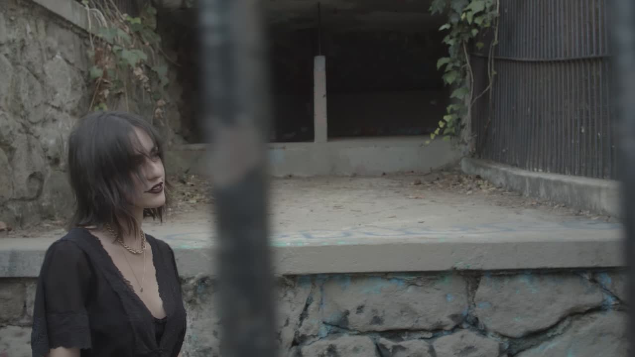 chica gótica con vestido negro detrás de las rejas de la celda de la prisión mirando a la cámara con una sonrisa