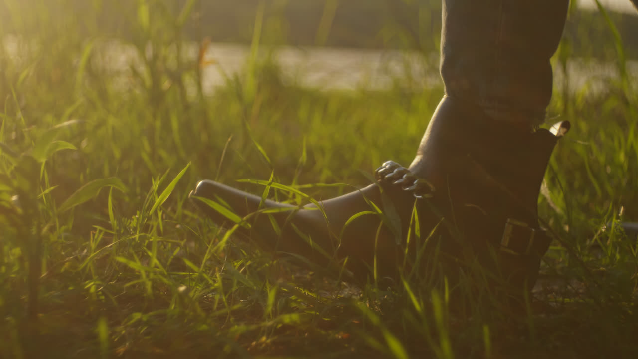 Woman's Foot in Boots on Grass by a River at Sunset