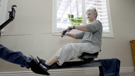 senior woman on a rowing machine at home - sliding view