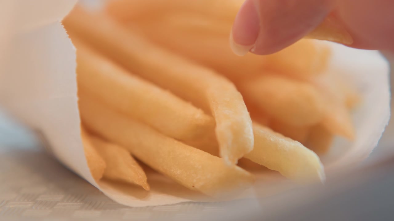 Primo piano ravvicinato dal basso che mostra patatine fritte dorate che riempiono un sacchetto di carta bianco, con un breve movimento della mano e forme che si assestano, luce calda e diffusa, consistenza croccante e fascino da snack informale