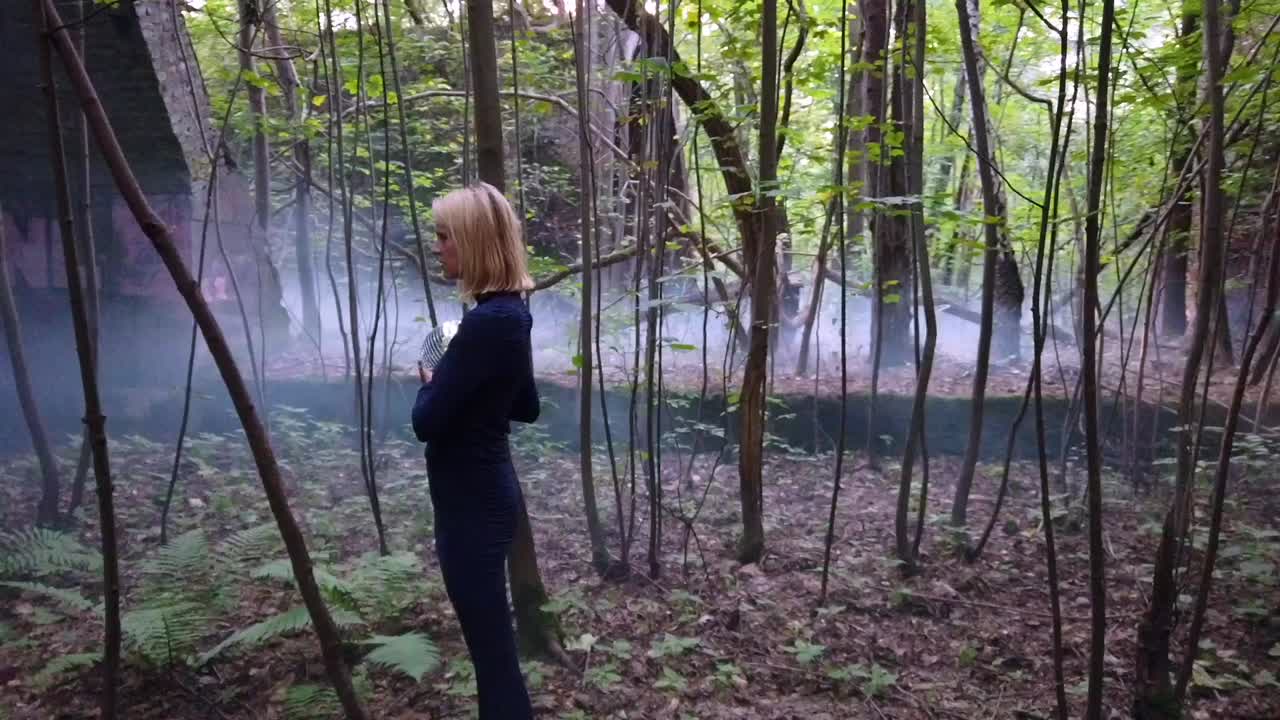 Spectacular slow motion cinematic shot of a blond weird girl with a mirror ball in a blue dress stand lonely in a foggy forrest. Foto video shoot on lost places in nature 1080, 24p by Philipp Marnitz