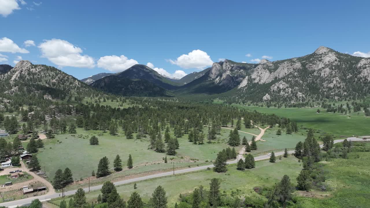 Flygfoto över idylliskt landskap av Klippiga bergen nära Estes Park, Colorado, USA, med en landsväg och gröna fält en solig sommardag