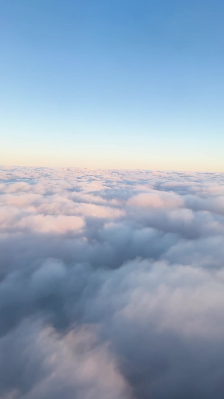 A serene aerial view of fluffy clouds illuminated by sunrise over Auckland, New Zealand, captured from an airplane