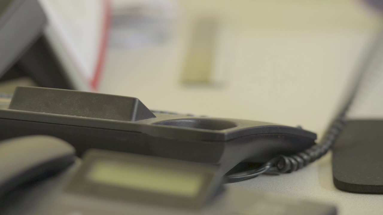 рука поднимает черный офисный телефон, быстро набирает номер, размытый фон