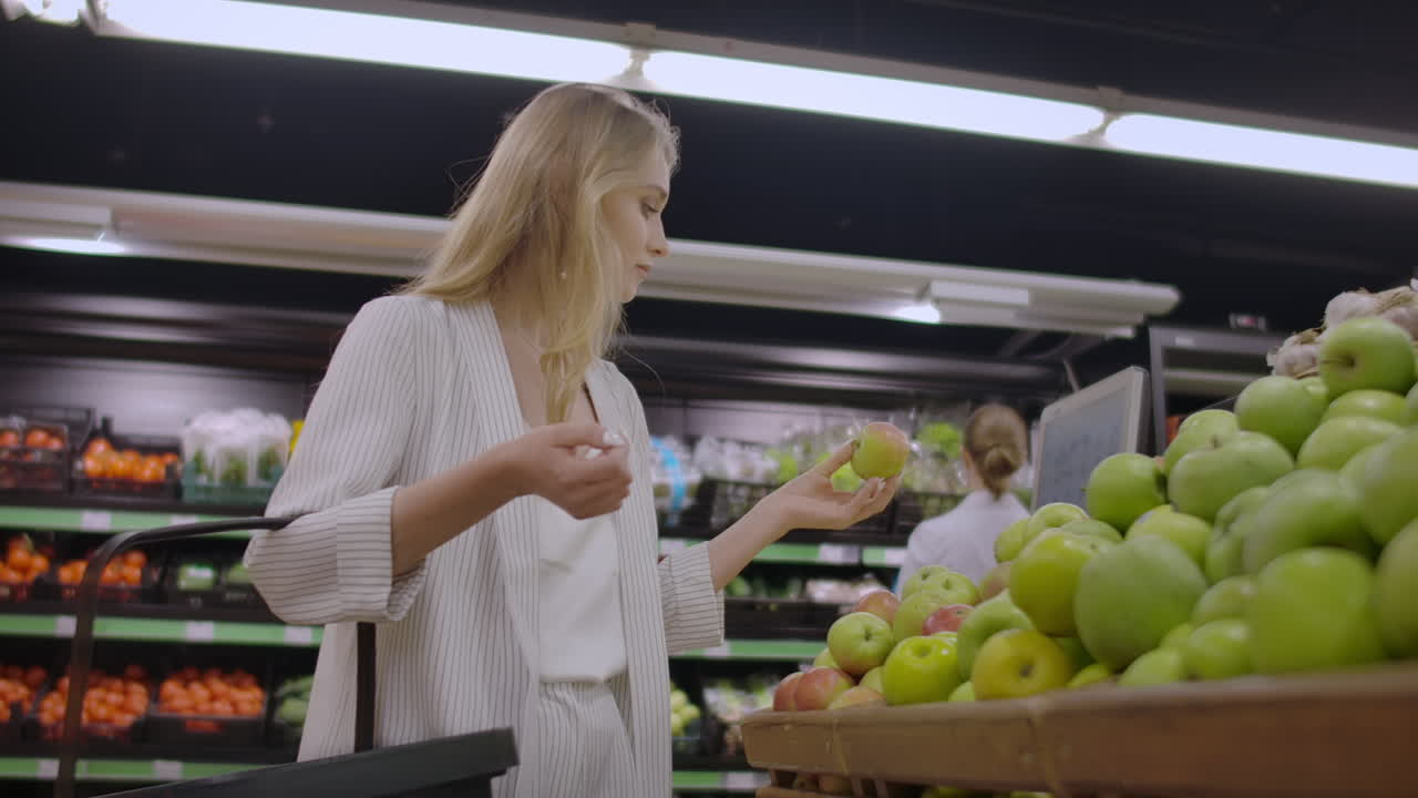 Attractive young woman choosing apple at fruit vegetable supermarket marketplace