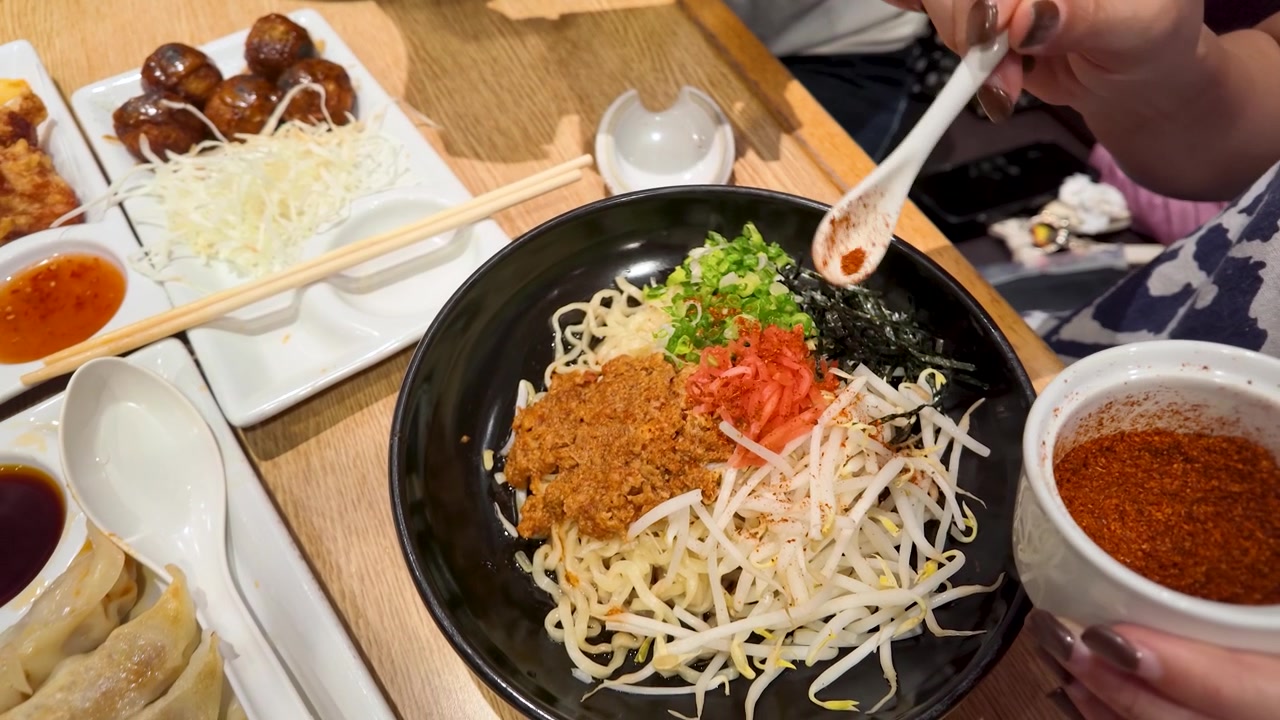 Primo piano delle mani che spargono peperoncino rosso in polvere sul ramen con germogli e carne di maiale macinata.