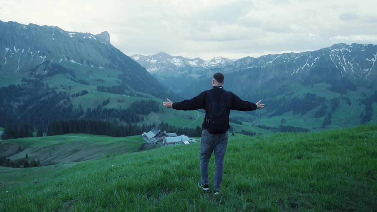 A young man hikes in the mountains and enjoys the beautiful view, green meadow and summertime